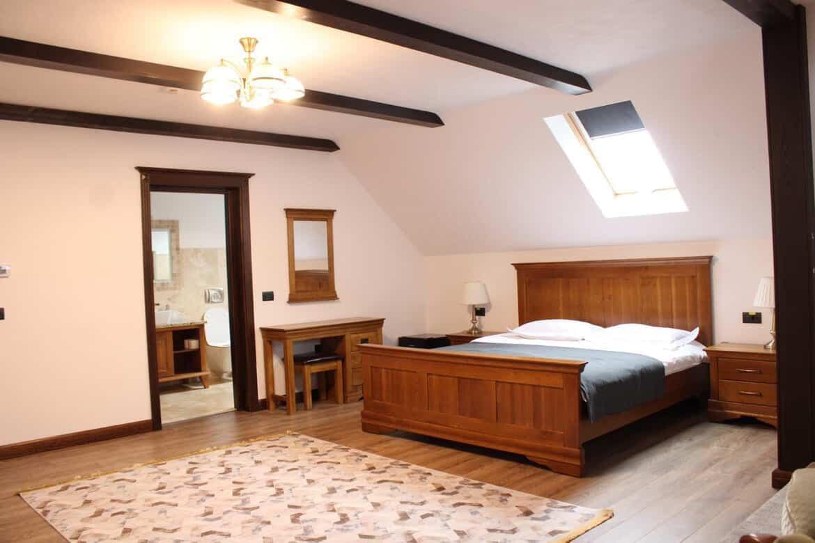 Dormitor elegant la mansarda cu pat king-size si mobilier din lemn masiv